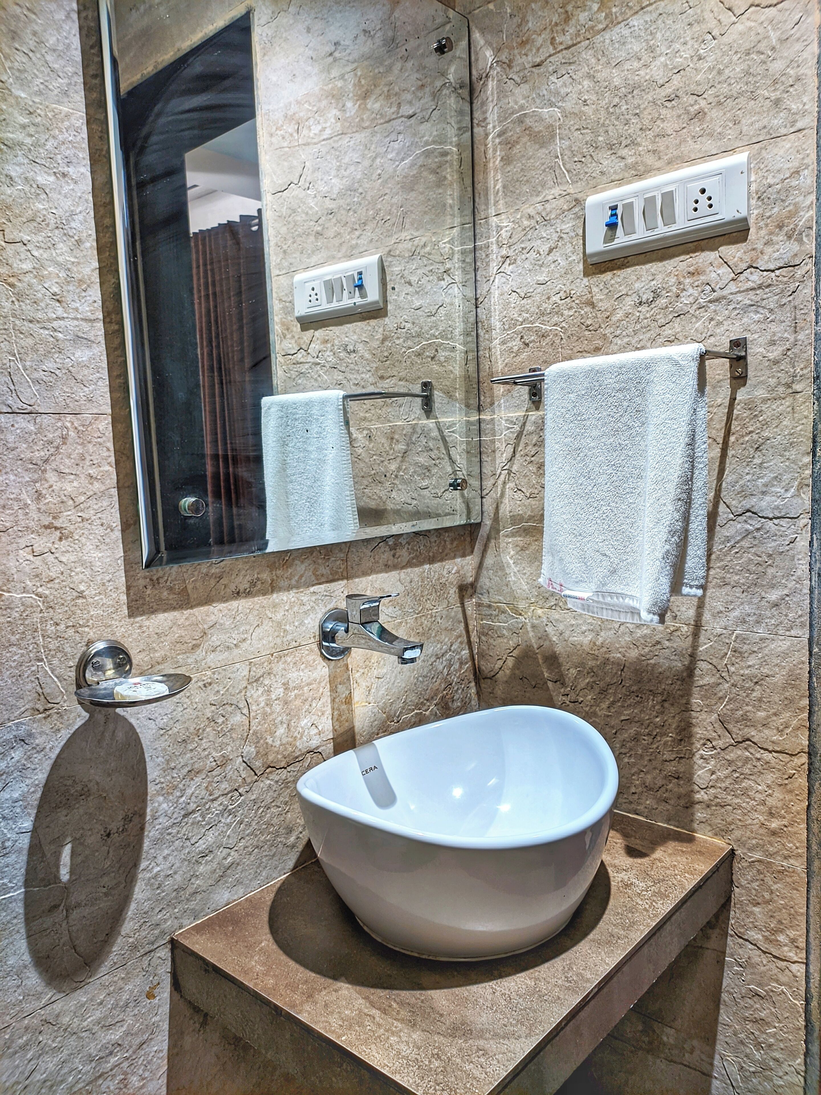 Un baño con un espejo grande, un lavabo, un perchero para toallas y un enchufe en la pared.
