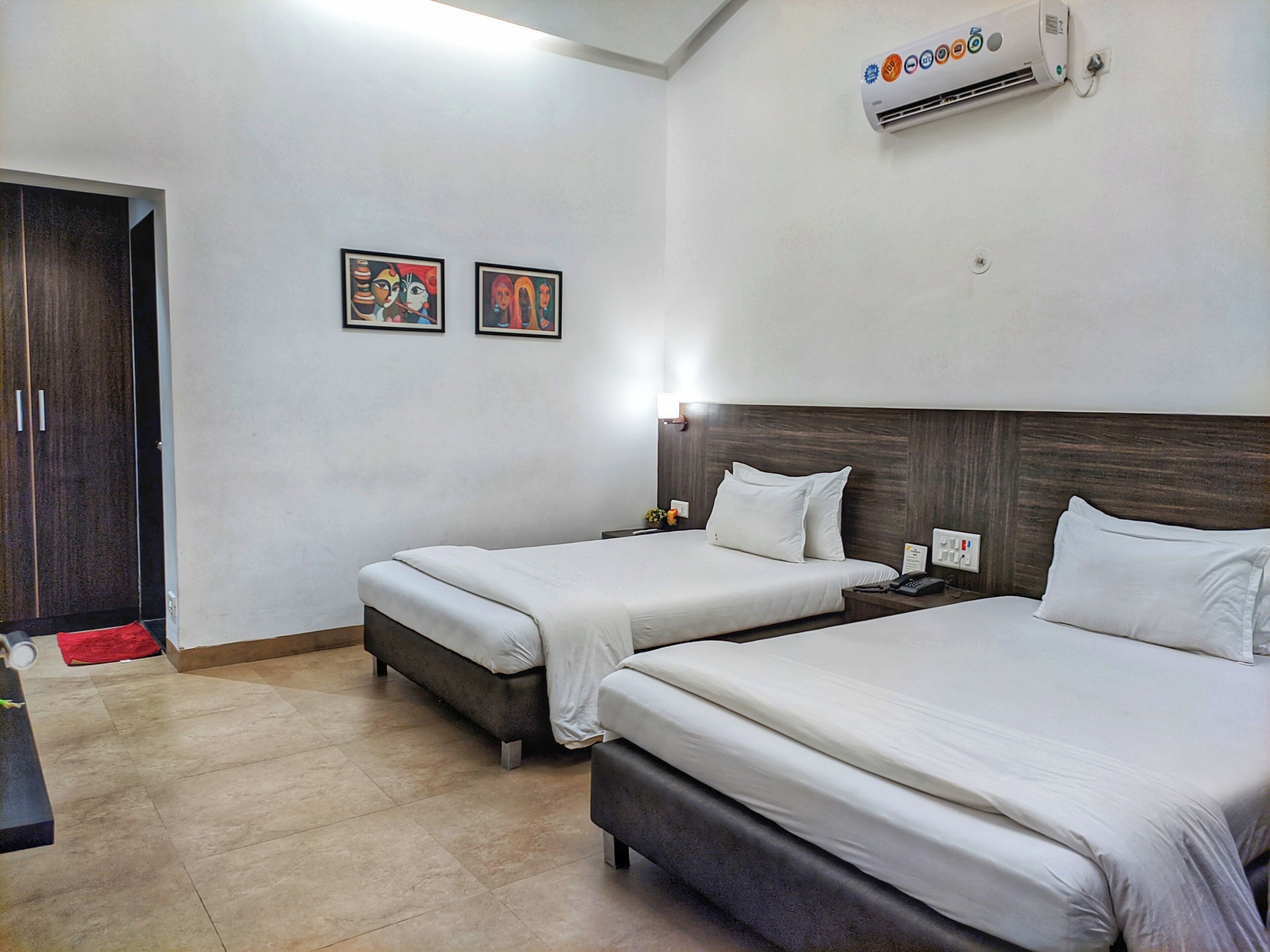 Habitación de hotel con dos camas, un armario, un tapete rojo y dos obras de arte enmarcadas en la pared.