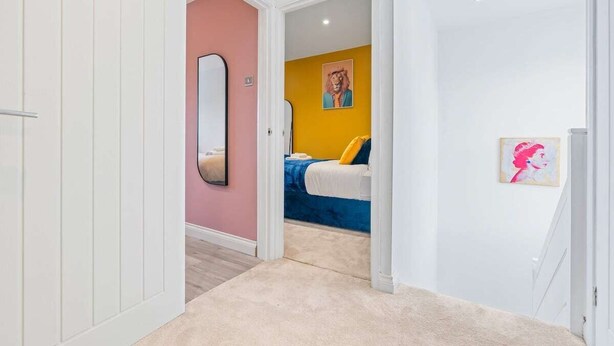 Un couloir menant à une chambre à coucher, où se trouvent un lit, un miroir et des œuvres d’art accrochées aux murs.