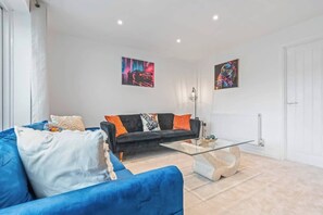 Una sala de estar moderna con un sofá negro, un sofá azul y una mesa de centro de vidrio.