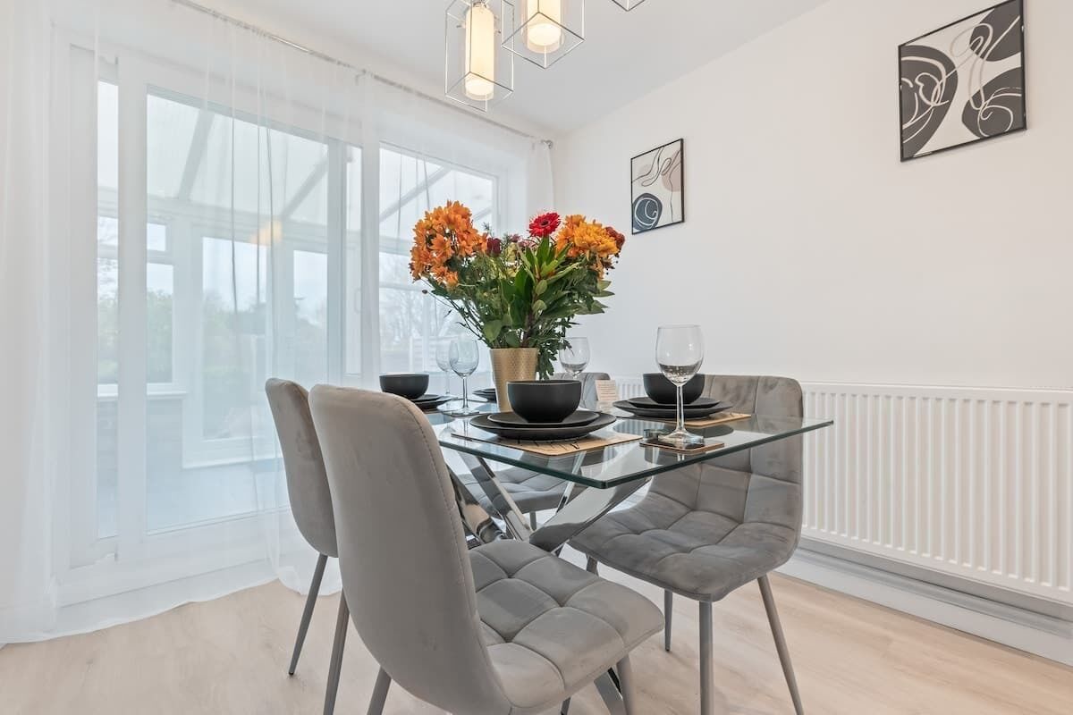 A modern dining area with a glass table, grey upholstered chairs, and a vase of flowers.