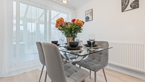 A modern dining area with a glass table, grey upholstered chairs, and a vase of flowers.