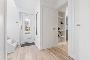 Un pasillo con una puerta blanca, una escalera y un estante empotrado con marcos de fotos.