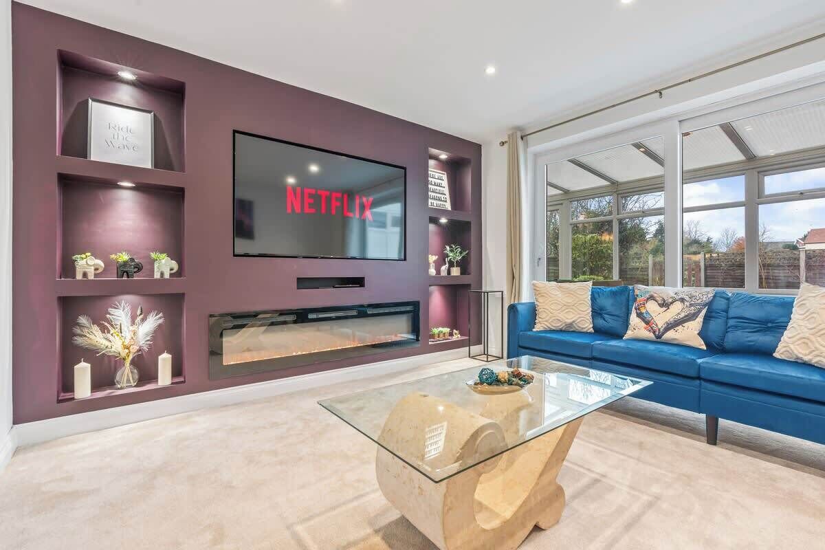Un salon moderne avec un téléviseur à écran plat fixé au mur, un canapé bleu, une table basse en verre et une cheminée.