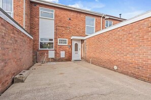 A brick building with a garage door, a small door, and a concrete driveway. - Dunchurch Home|Free Parking|Contractors & Families (Dunchurch)