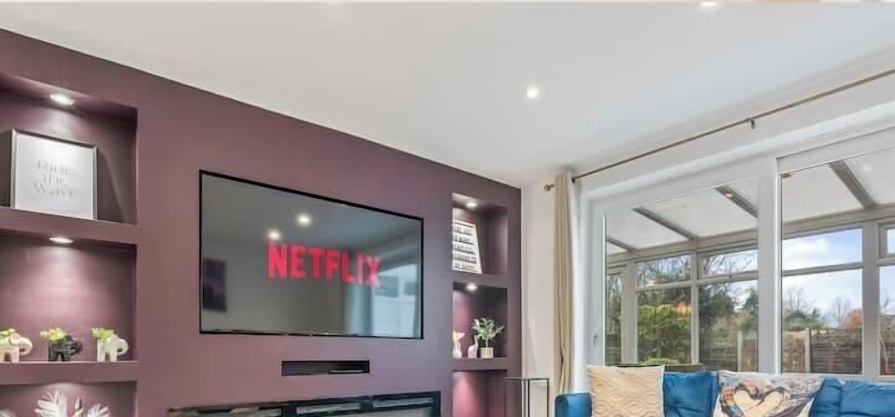 A living room with a large flat-screen TV mounted on the wall, a sofa, and a window with a view.