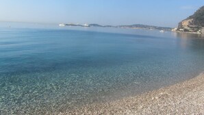 Una vista chiara sulla costa, con spiaggia di ciottoli, mare calmo e terraferma in lontananza con edifici.