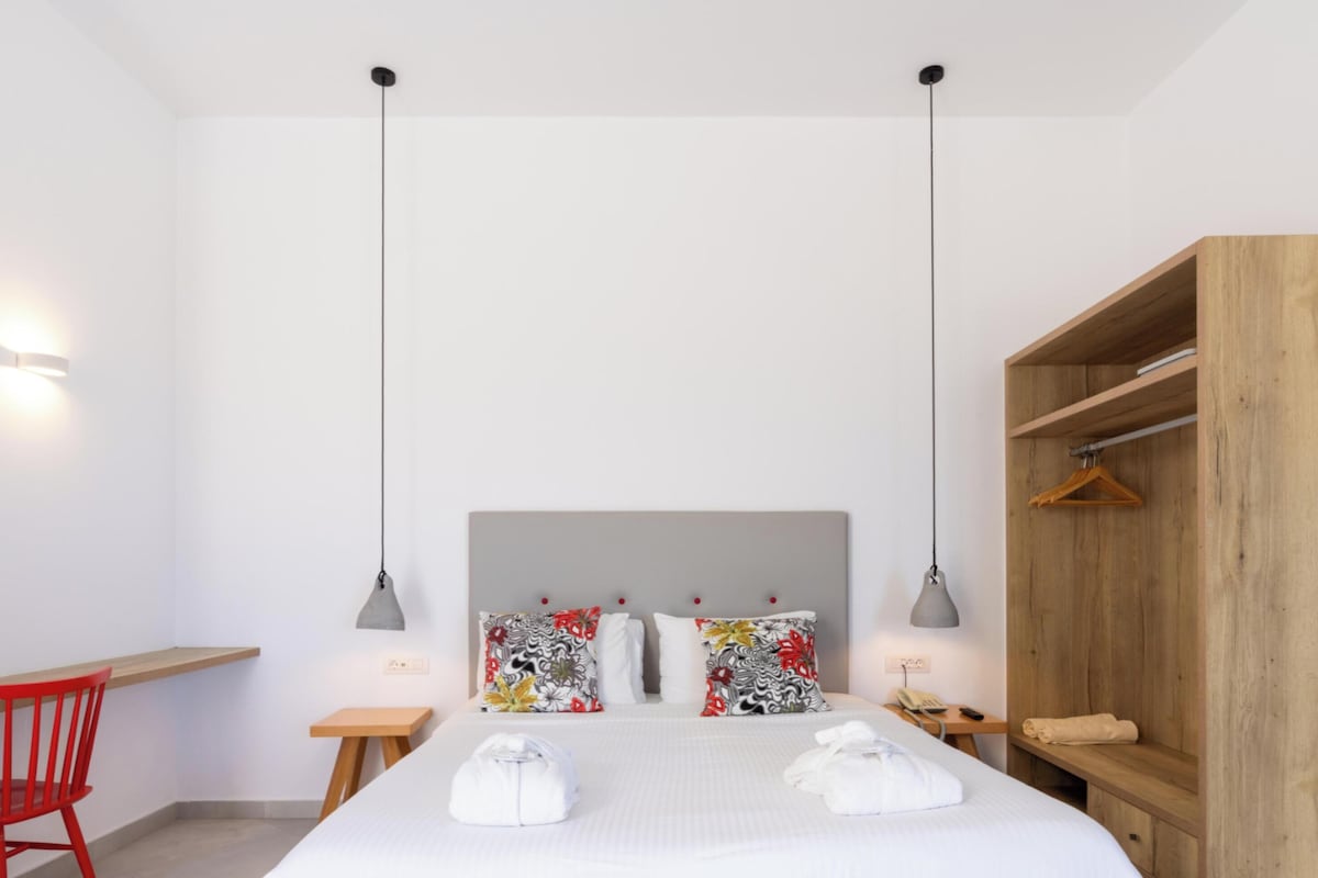 A hotel room with a bed, a desk, a chair, a wardrobe, and two pendant lights.