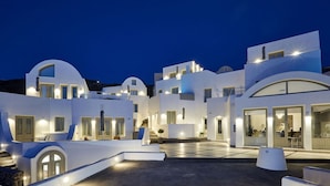 A modern white building with multiple levels and balconies, featuring large windows and a spacious courtyard. - Hotiday Santorini Oia (Santorini)
