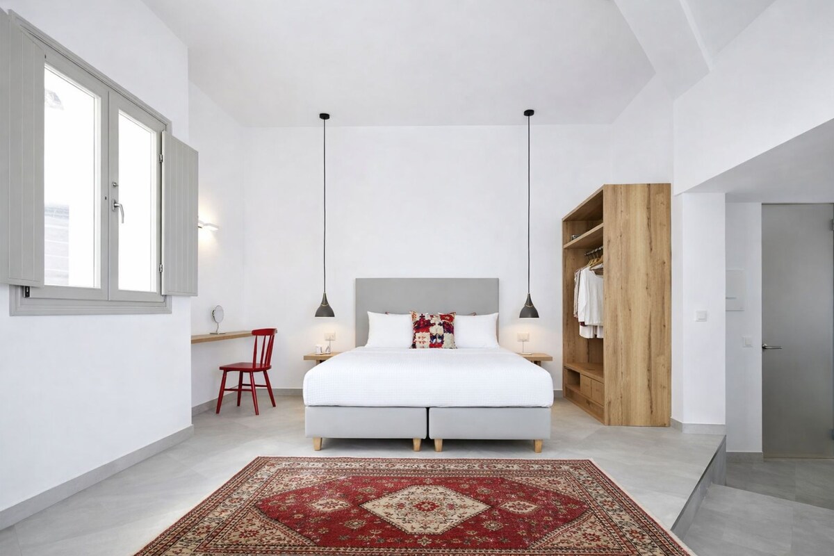 A bedroom with a bed, a red chair, a wooden wardrobe, and a red patterned rug.