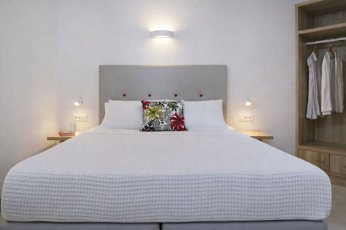 A large bed with a white quilt, a colorful pillow, and two bedside lamps.