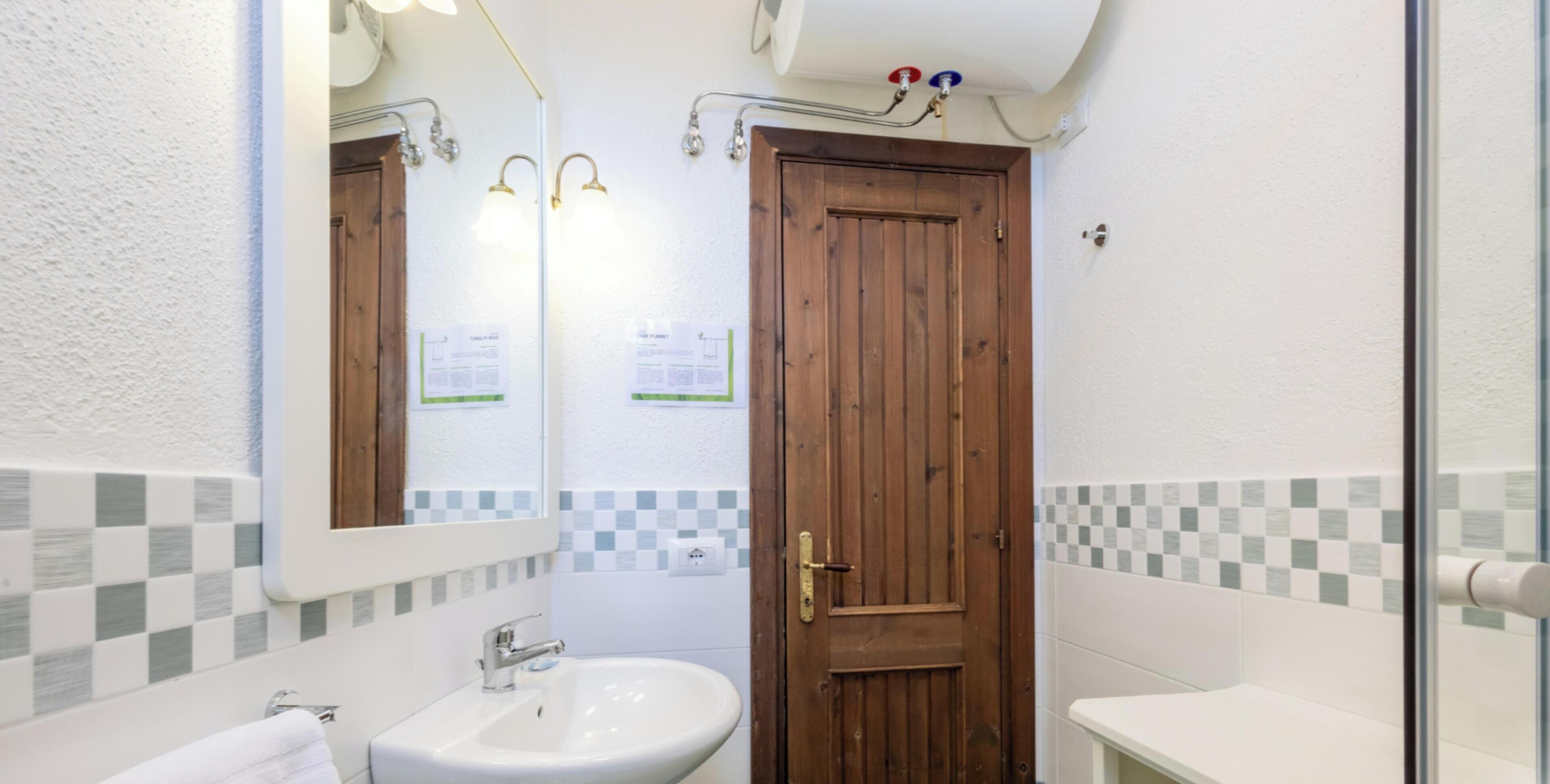 Een badkamer met een houten deur, een witte wastafel en een spiegel met verlichting.