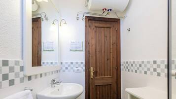 Un bany amb una porta de fusta, un lavabo blanc i un mirall amb il·luminació.