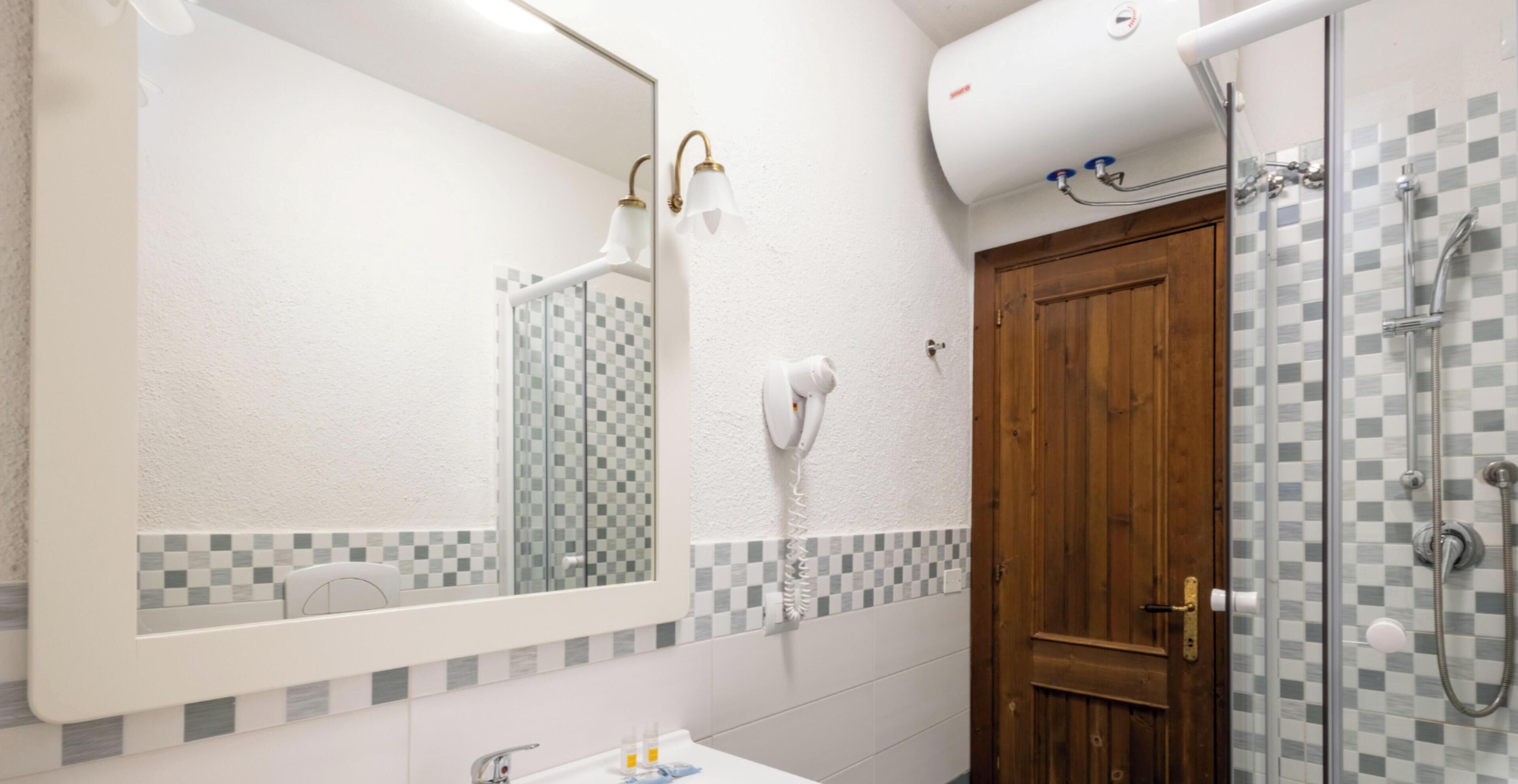 Un baño con un espejo grande, un lavamanos blanco, un dispensador de toallas, una ducha con puerta de vidrio y una puerta de madera.