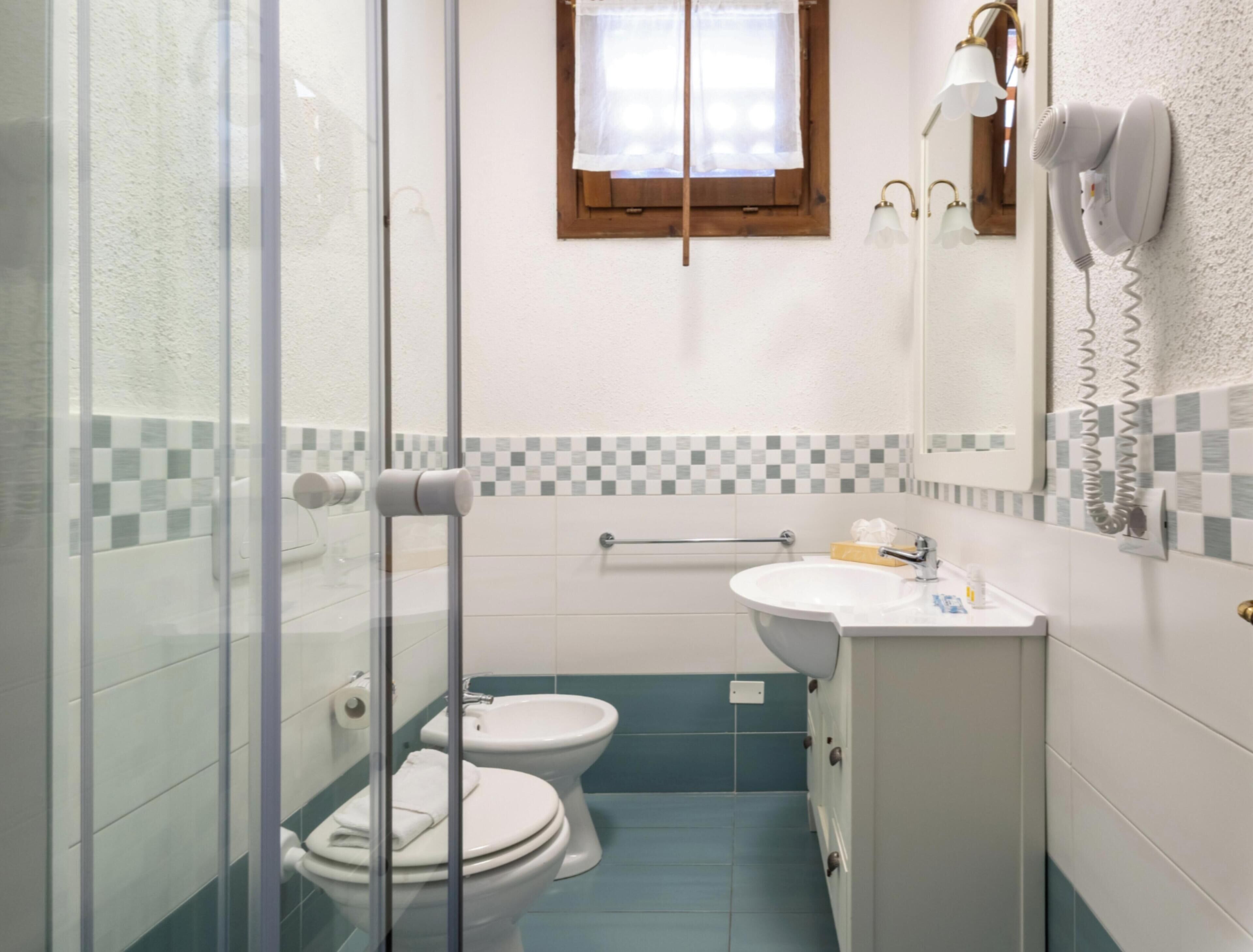 Une salle de bain équipée d’une douche à parois de verre, de toilettes, d’un bidet, d’un lavabo et d’un miroir avec un téléphone.
