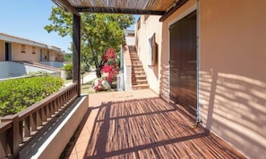 Un espacio al aire libre cubierto con una terraza de madera, una escalera y un edificio con puerta metálica.