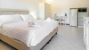 A hotel room with a bed, a desk, a refrigerator, and a cabinet. - Hotiday Punta Sardegna (Costa Serena)
