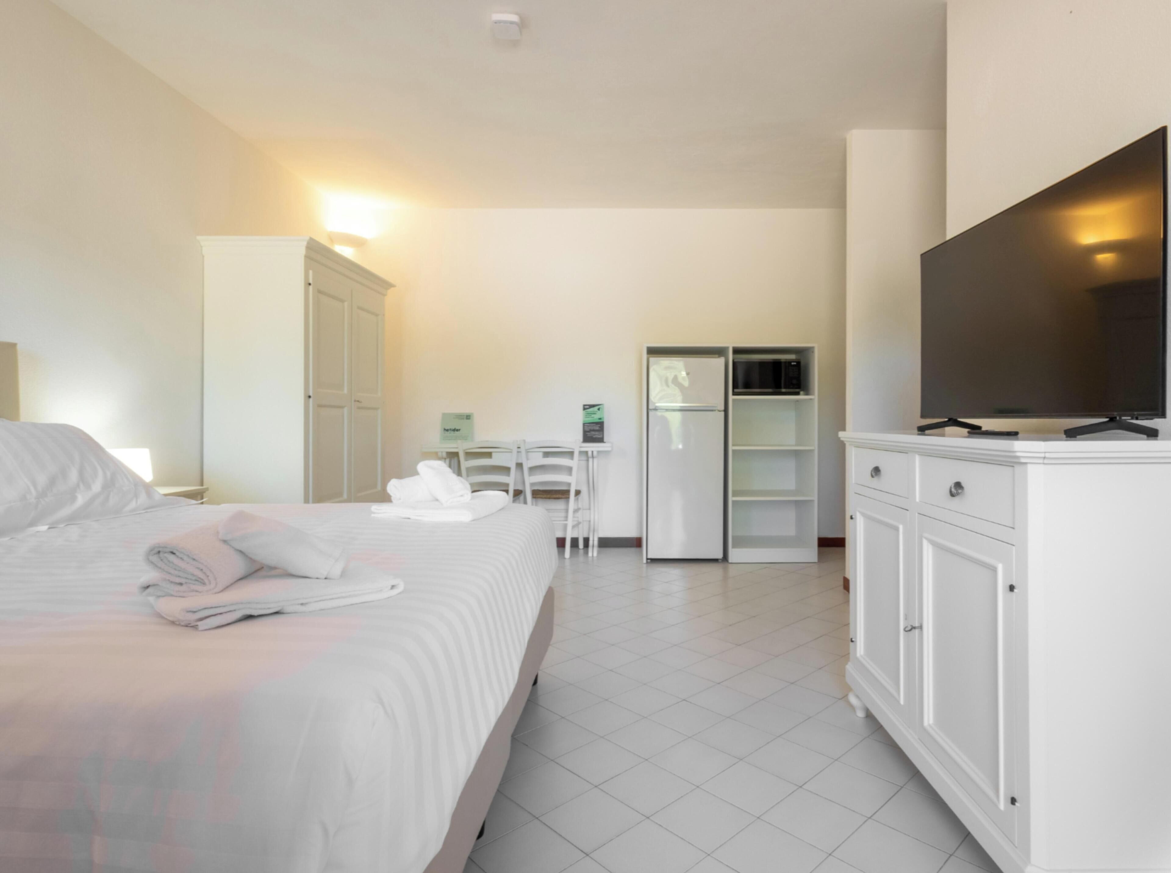 Une chambre d’hôtel équipée d’un lit, d’un bureau, d’un réfrigérateur et d’une télévision.