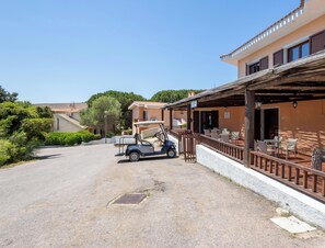 A building with a covered patio area, a golf cart, and a paved driveway. - Hotiday Punta Sardegna (Costa Serena)