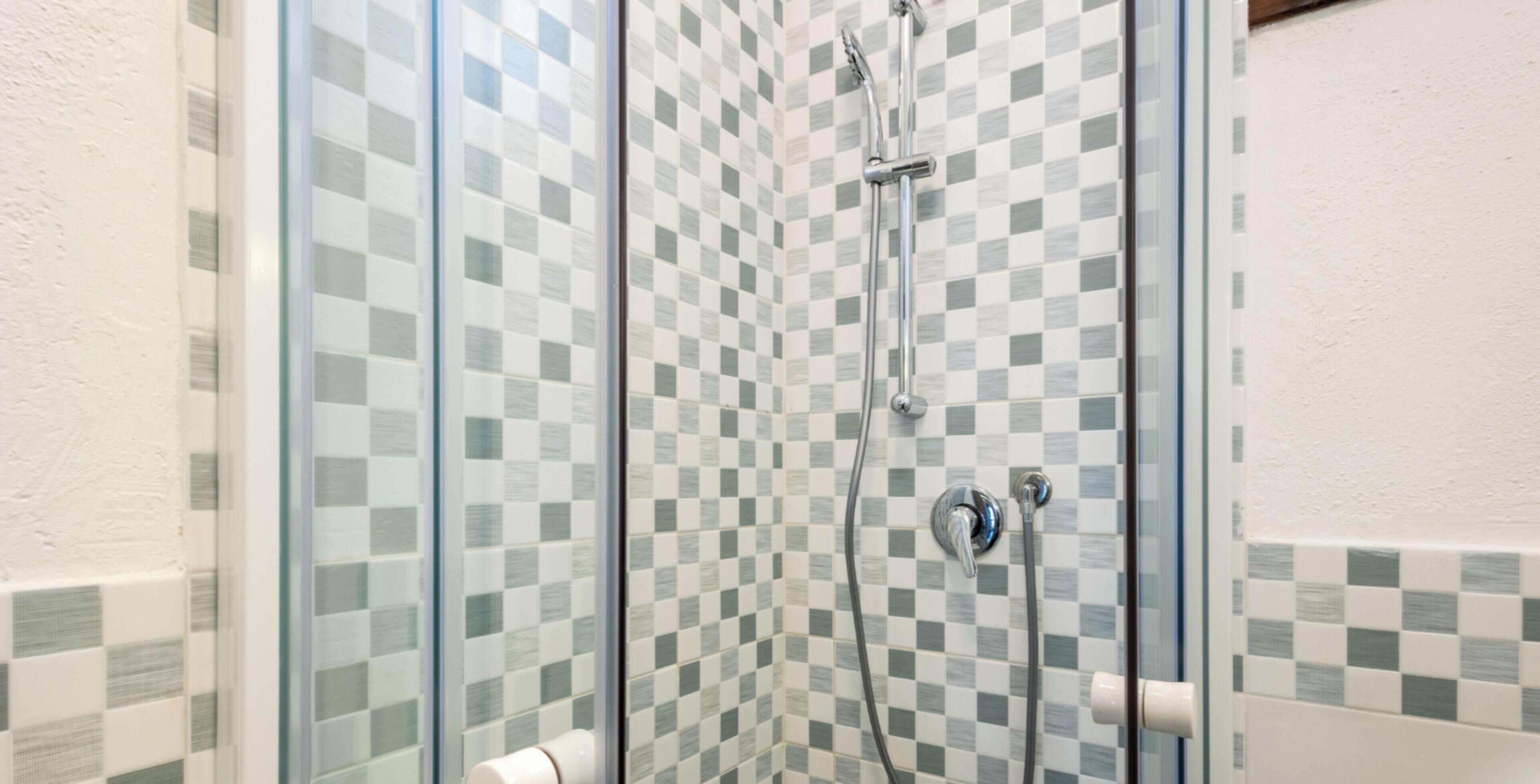 Um chuveiro com paredes de azulejo xadrez, protegido por um vidro.