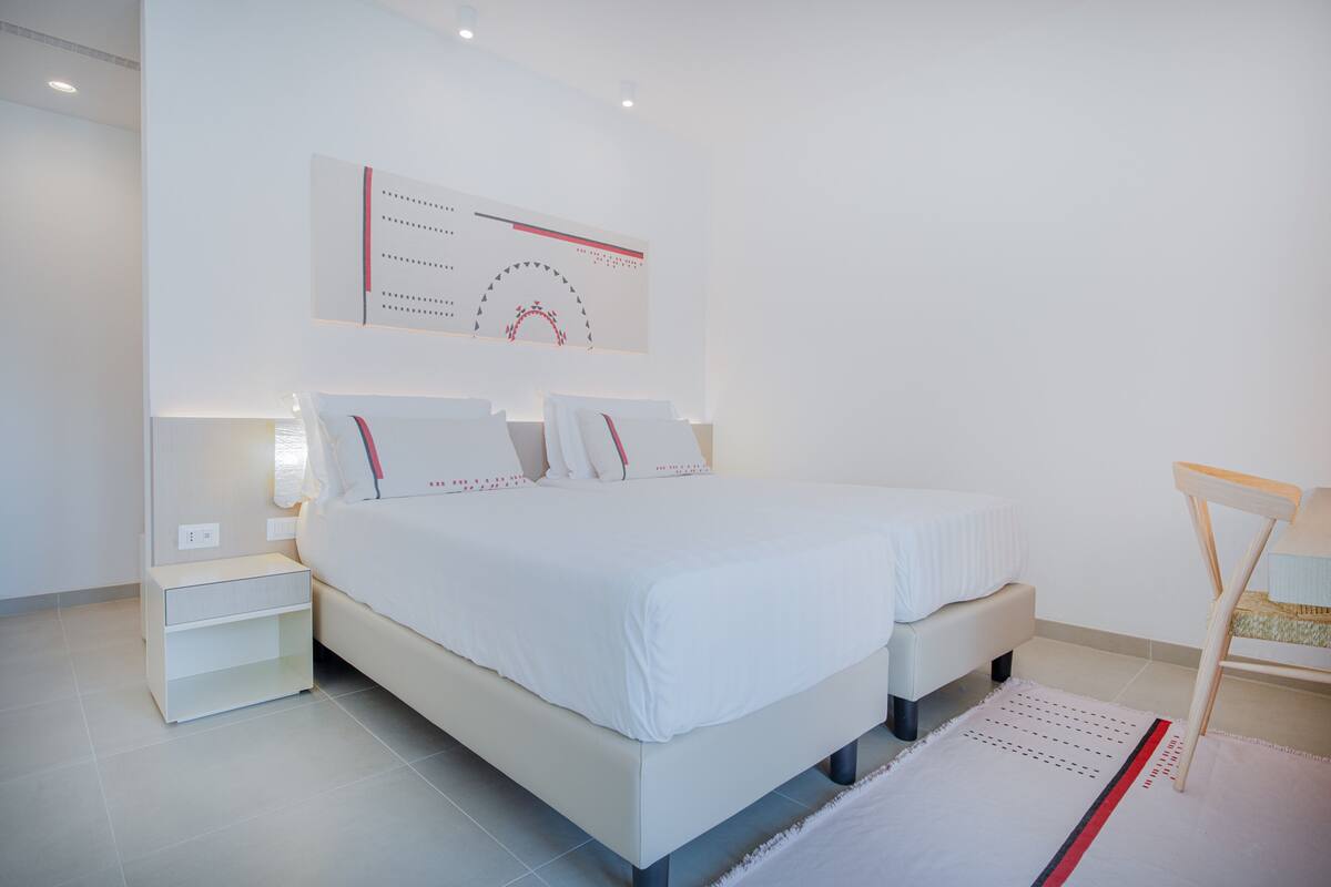 A modern bedroom with a large bed, bedside tables, and a wall-mounted artwork.