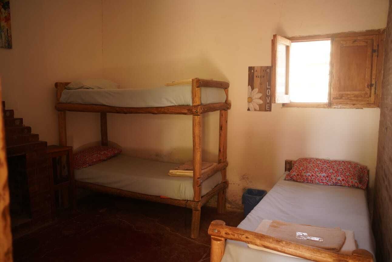 A room with a bunk bed, a single bed, a window with a wooden frame, and a wall-mounted sign.
