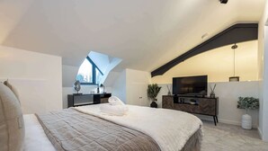 A bedroom with a large bed, a TV, a desk, and a window.