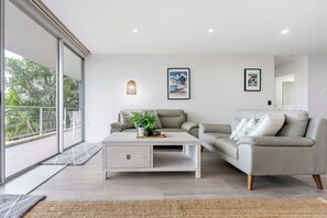 Ein modernes Wohnzimmer mit einer Couch, einem Couchtisch und einem großen Fenster mit Blick auf Grünflächen.