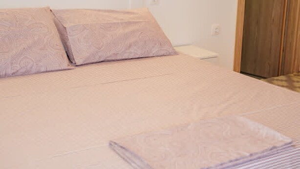 A neatly made bed with a patterned bedspread and pillows, a wooden nightstand with a lamp, and a wooden door. - Filippos Traditional Villa - Pool Garden Gem (Finiq)