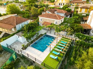 A residential area with a swimming pool, surrounded by houses with red-tiled roofs and lush greenery. - Filippos Traditional Villa - Pool Garden Gem (Finiq)