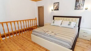 Ein Schlafzimmer mit Holzboden, einem Bett mit gestreifter Bettdecke, einem Holz-Kopfteil und zwei an der Wand befestigten Leuchten.