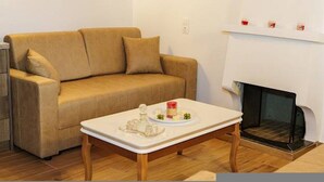 Ein Wohnzimmer mit einem beigefarbenen Sofa, einem weißen Couchtisch mit Kerze und Blumen sowie einem Kamin.