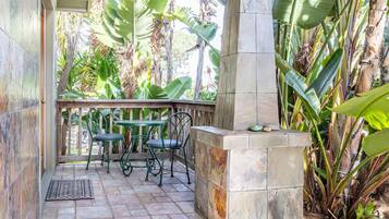An outdoor patio with a tiled floor, two green metal chairs, a small round table, and a stone planter with a few rocks.