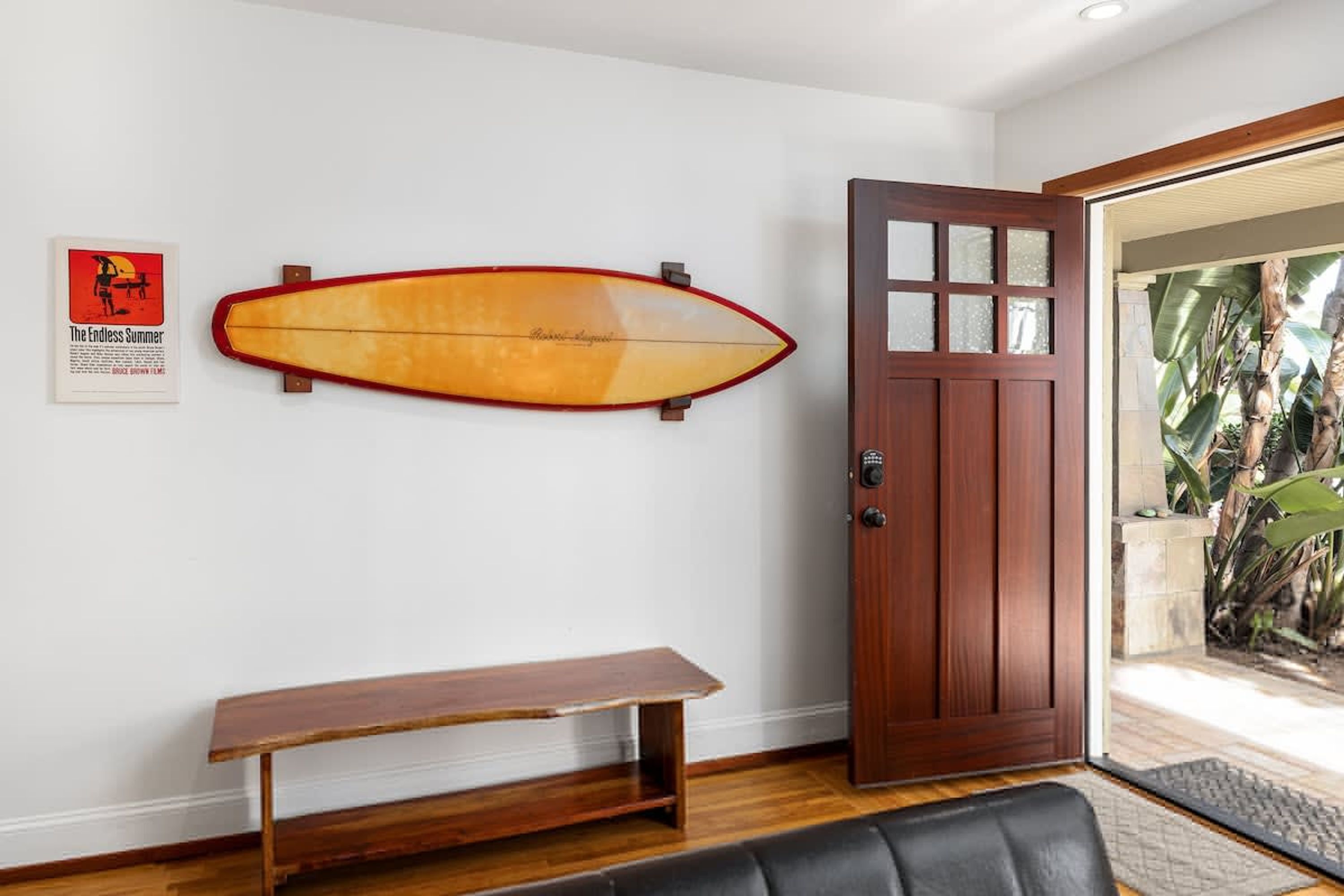A room with a wooden bench, a surfboard, a door, and a poster on the wall.