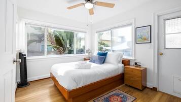 A bedroom with a bed, a ceiling fan, a nightstand, a dresser, and a window with a view of palm trees.
