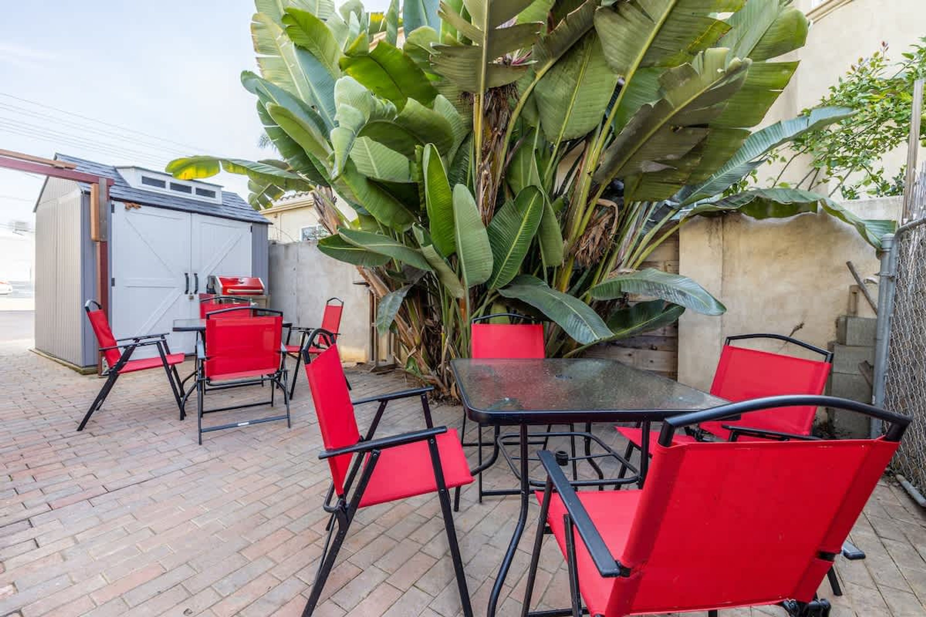 Eine Terrassengruppe im Freien mit roten Stühlen und einem Tisch, umgeben von großen Bananenpflanzen und einem Metallzaun.