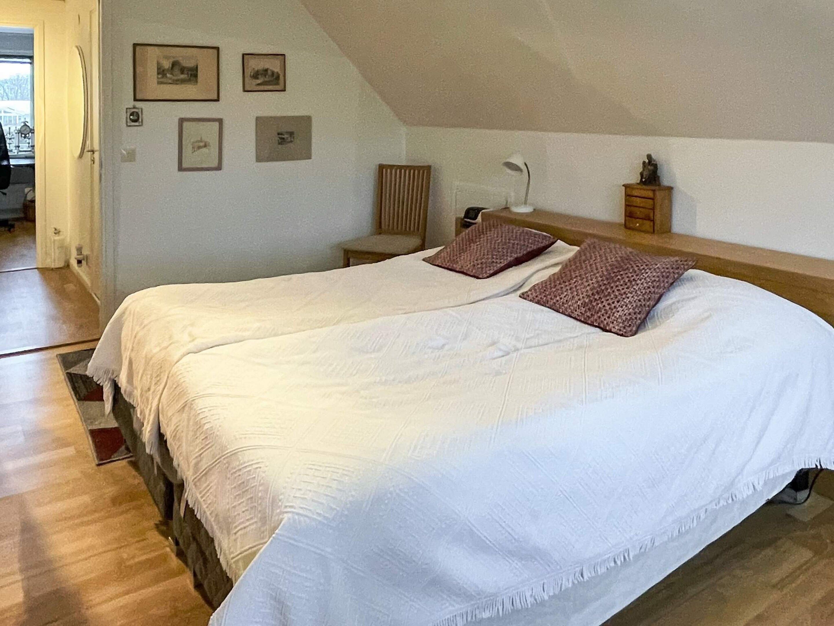 A bedroom with a large bed, two pillows, a nightstand, a lamp, and framed pictures on the wall.