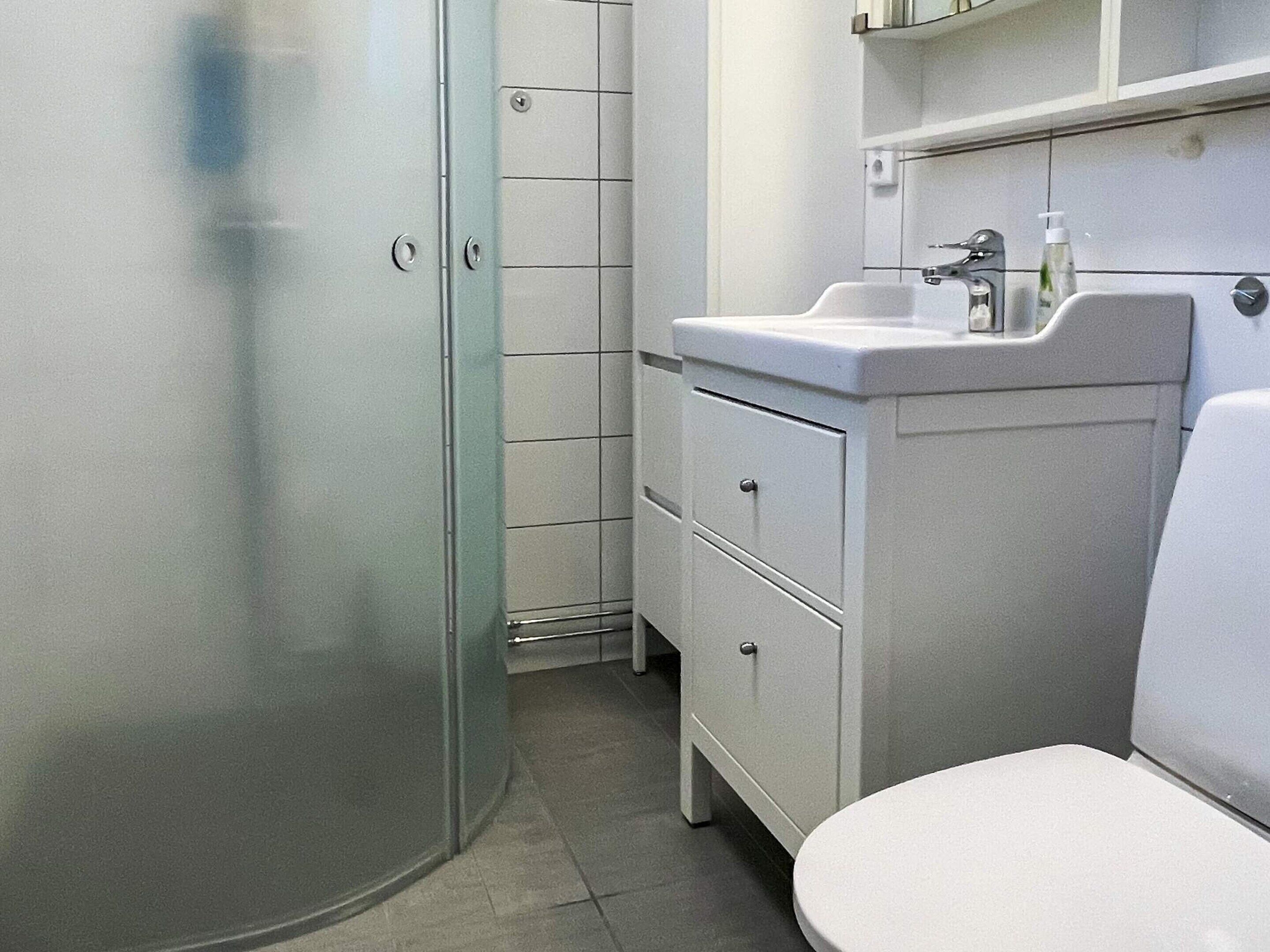 A bathroom with a glass shower enclosure, a white sink, and a toilet.