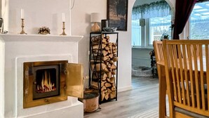 A living room with a fireplace, a wooden bench, a rug, and a stack of firewood. - 4 Star Holiday Home in Bergkvara (Bergkvara)