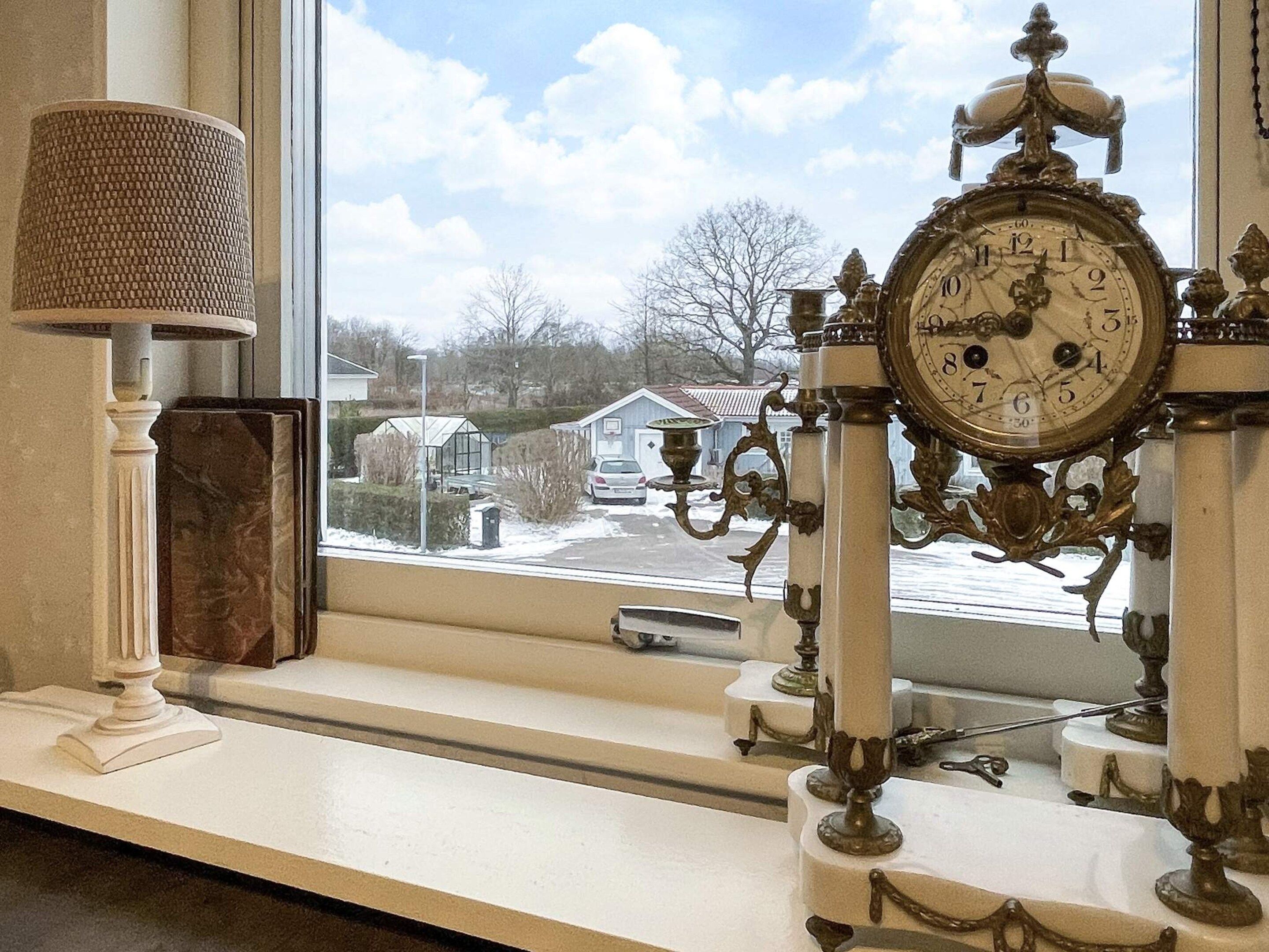 Una habitación con un ventanal grande, un reloj decorativo y una lámpara en un estante.