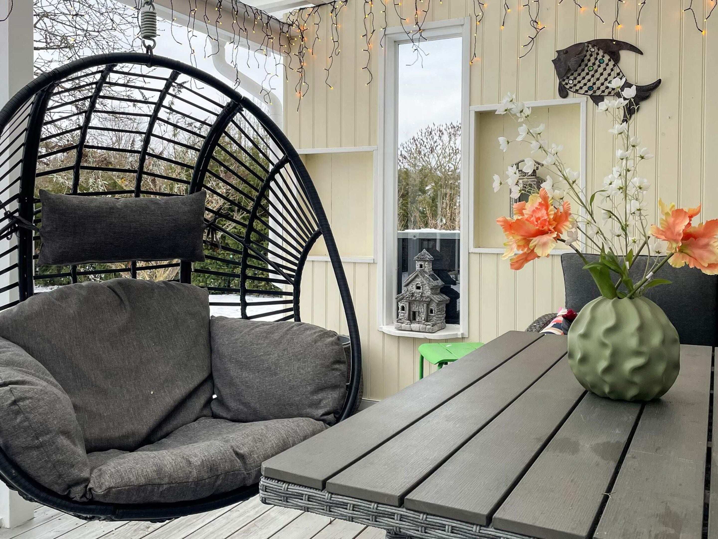 A cozy outdoor seating area with a wicker chair and a table, decorated with string lights and a vase of flowers.
