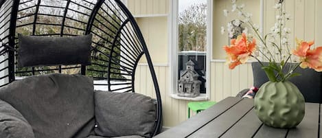 A cozy outdoor seating area with a wicker chair and a table, decorated with string lights and a vase of flowers.