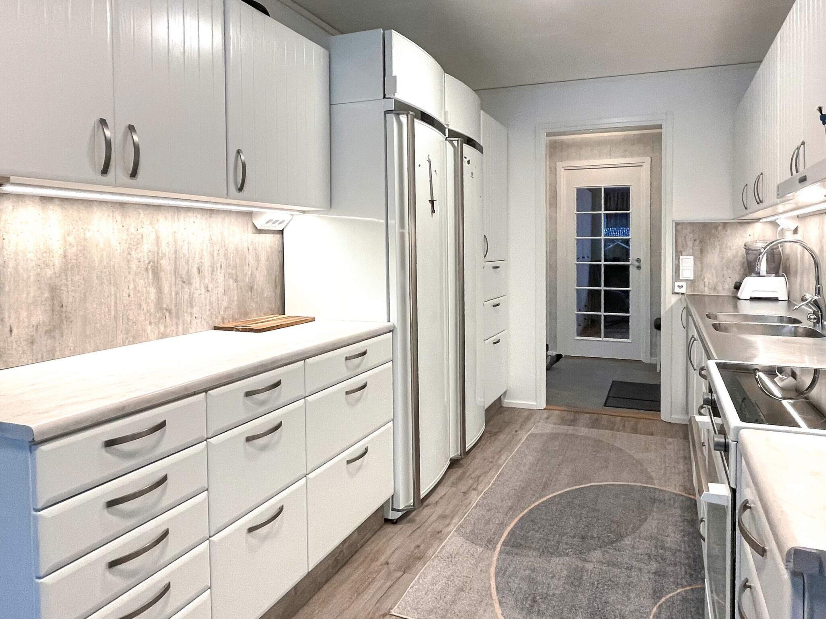 A modern kitchen with white cabinetry, a stainless steel refrigerator, and a built-in oven.