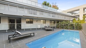 Una piscina interior moderna con superficie de agua azul cristalina, rodeada por una solana empavedada. Hay sillones de descanso y una tumbona junto a la piscina.
