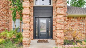 A brick house with a dark front door, a small porch, and a window above the door.