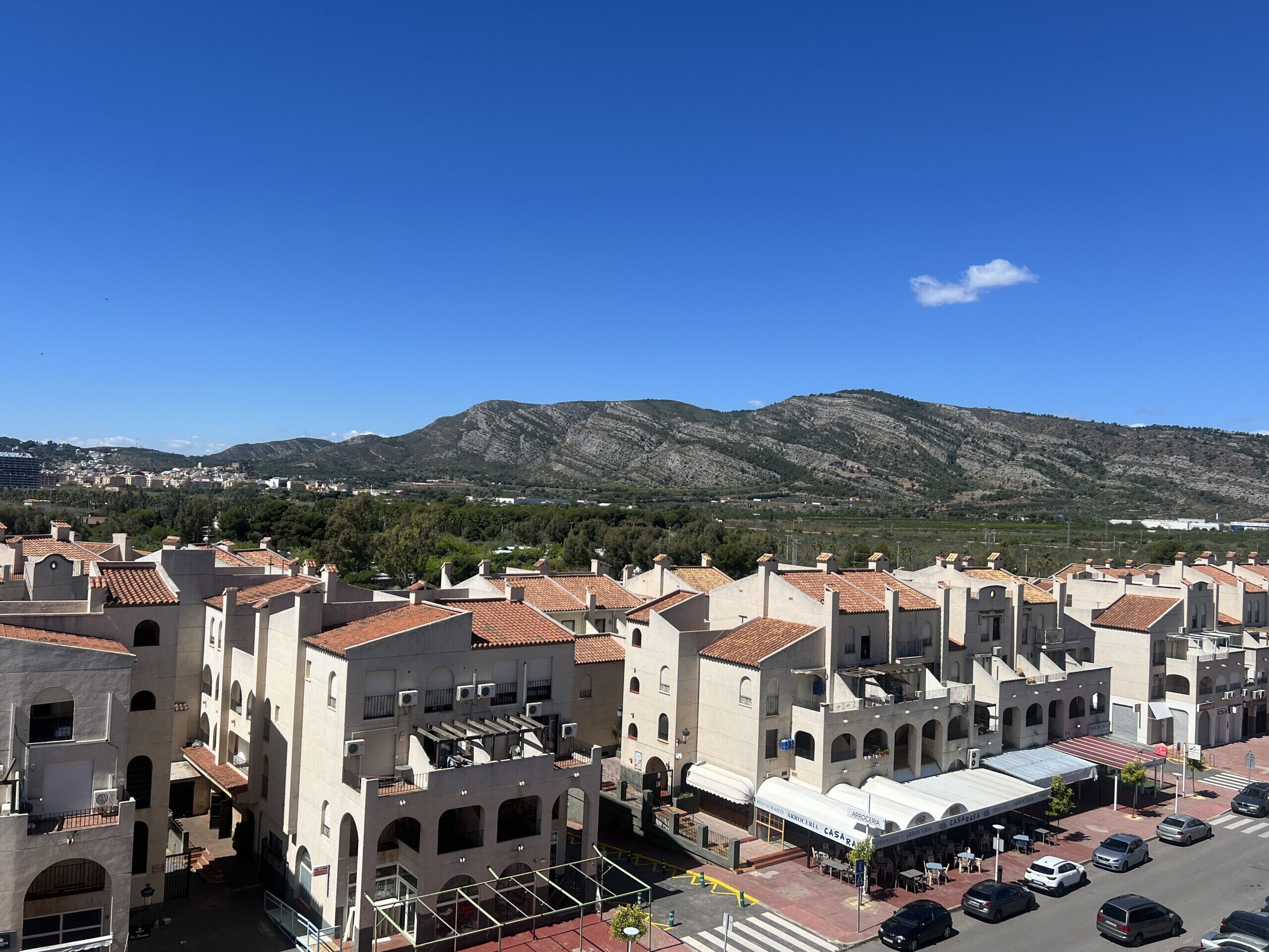 Vista de un pueblo con edificios de techos de tejas rojas y montañas al fondo.