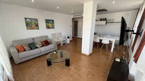 Un soggiorno moderno con un divano grigio, un tavolino da caffè in vetro e un'area pranzo con tavolo e sedie bianche.