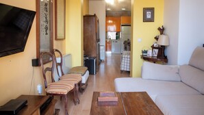 Un soggiorno con divano, poltrone, tavolino, televisione e una cucina sullo sfondo.