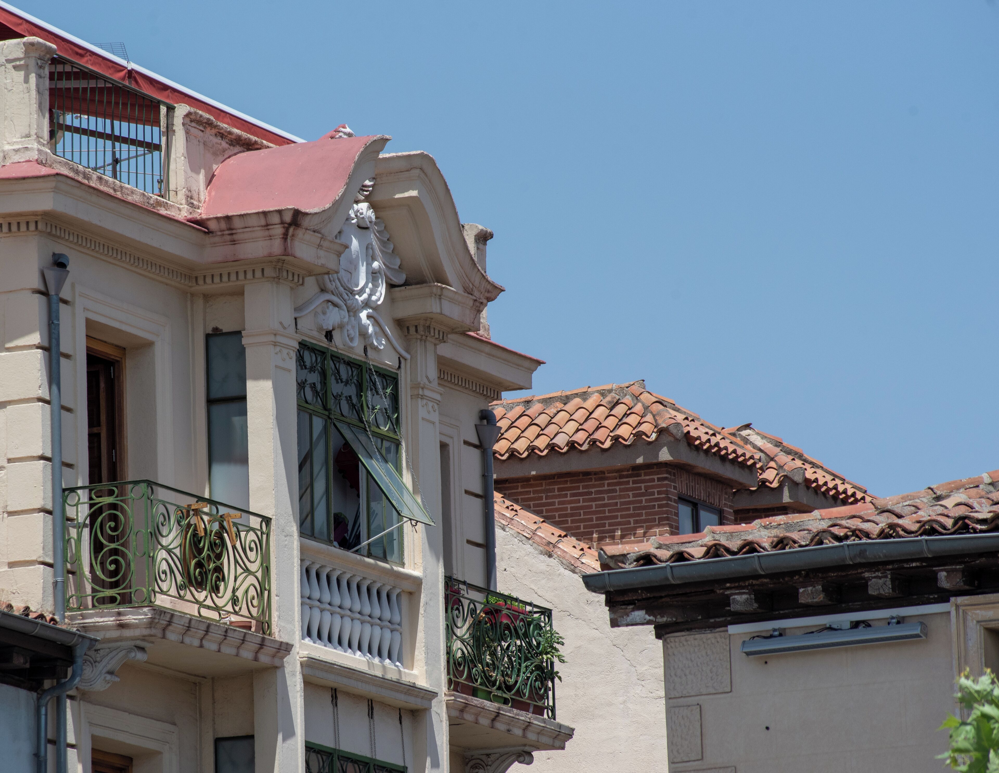 Ein Gebäude mit einer klassizistischen Fassade, einem Balkon mit aufwendigen Eisengeländern und einem Ziegeldach.