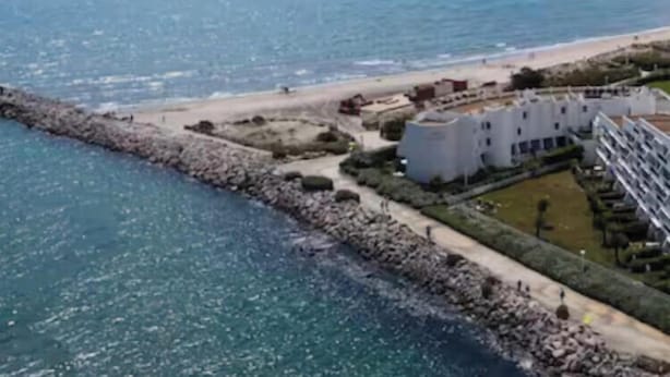 Un hotel sul litorale con un promontorio roccioso, una spiaggia sabbiosa e vista libera sul mare.